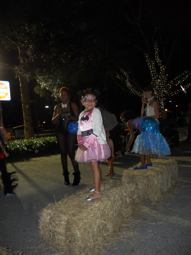 Girl in pink batman costume and white coat standing on hay bales